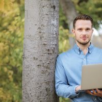 Mann med bærbar pc ved tre