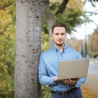 Mann med bærbar pc ved tre